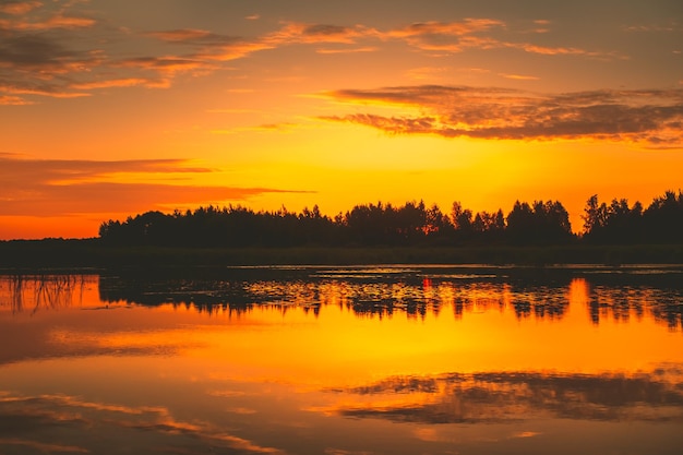 Por do sol laranja brilhante sobre nuvens douradas do lago