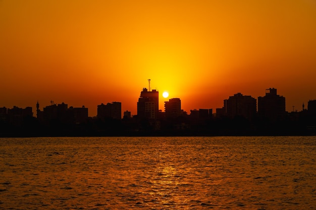 Pôr do sol laranja no rio Nilo, o sol se esconde nos edifícios da cidade do Cairo