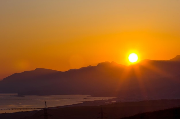 Pôr do sol laranja sobre montanhas no custo do mar