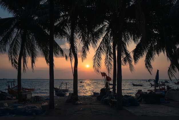 Pôr do sol na praia com coqueiros e barco de pesca