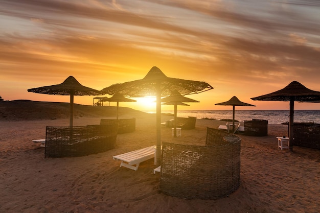 Pôr do sol na praia com guarda-sóis e espreguiçadeiras de palmeiras