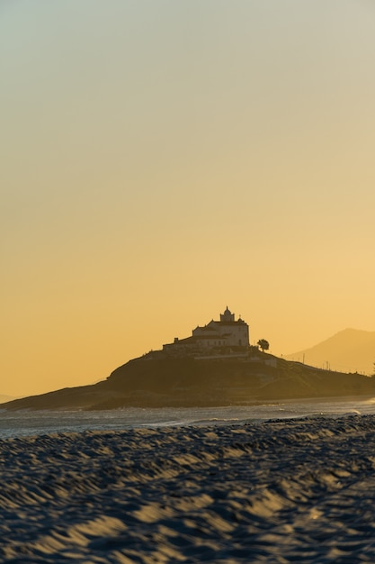 Foto pôr do sol na praia de saquarema no rio de janeiro, brasil. famosa pelas ondas e pelo surf. igreja no topo da colina. luz baixa.