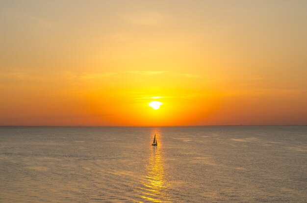 Pôr do sol no horizonte do mar do oceano, com um idiota de um veleiro na água refletida na luz.