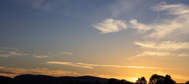 Pôr do sol sobre colinas silhueta nuvens espalhadas no céu O pôr do sol está no lado direito