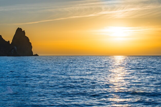 Pôr do sol sobre o mar azul com pedras e céu laranja