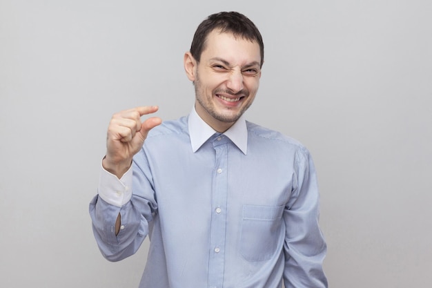 Por favor, me dê mais alguns. Retrato do empresário bonito com cerdas no clássico camisa azul clara em pé e implorando um pouco mais. tiro do estúdio interno, isolado no fundo cinza copyspace.