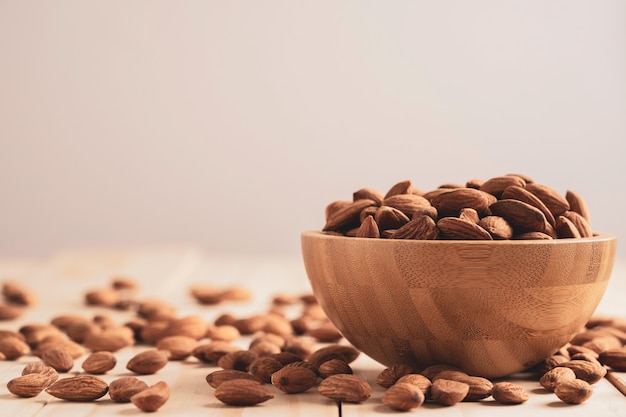 Porca de amêndoas em uma tigela de madeira e despeje na mesa com espaço de cópia. A noz de amêndoa é um alimento de dieta saudável com alto teor de proteína, baixo teor de gordura e aminoácidos essenciais.