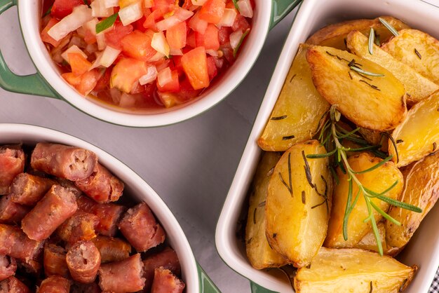 Foto porção de batatas assadas, linguiça e vinagrete