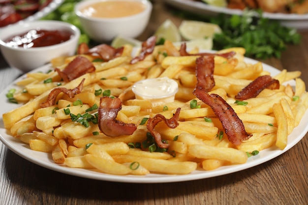 Foto porção de batatas fritas com bacon. alface, cebola verde, tomate, ketchup e maionese.