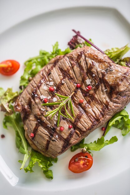 Porção de close-up de suculento bife de flanco de salada de legumes, sal, pimenta e alecrim na chapa branca.