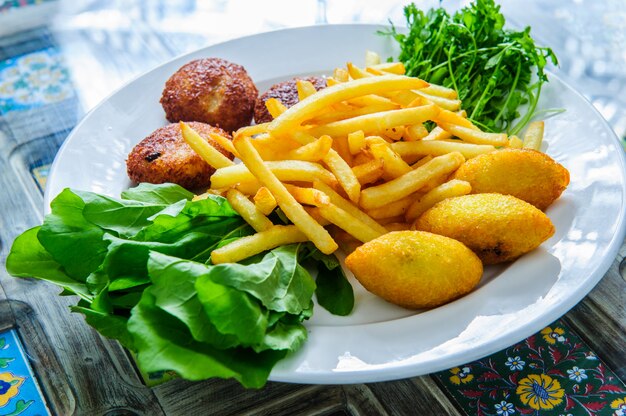 Porção de falafel e batatas fritas servidas em um prato preto com molho.