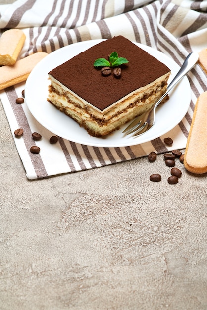 Porção de sobremesa tiramisu italiana tradicional e biscoitos savoiardi na mesa de concreto cinza