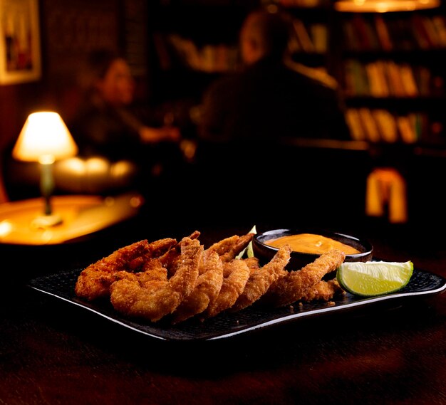 porção de tapas de camarão à milanesa com molho e fatias de limão de pub fundo desfocado