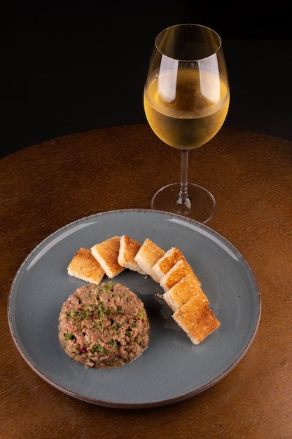 Porção de tártaro de carne crua com especiarias em fundo desfocado com copo de vinho branco vista superior