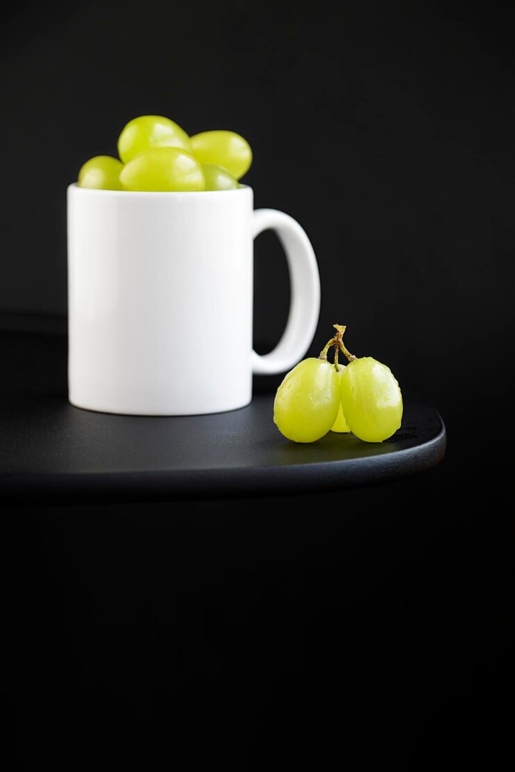 Porção de uvas verdes dentro de uma caneca branca sobre fundo preto
