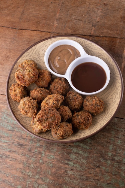 Porción de aperitivo de albóndigas de pastel de carne de tapas de pub o mini kibis kafta con mostaza negra y salsa de barbacoa en la vista superior de la mesa de madera rústica