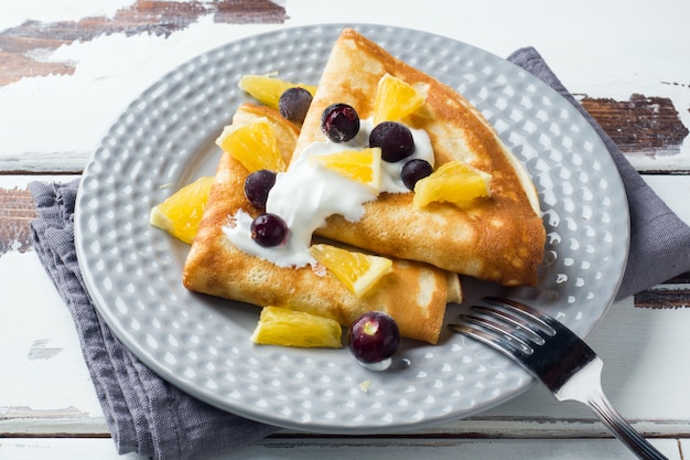 Una porción de crepes con las bayas y la crema en la placa.