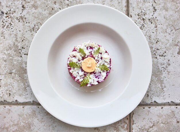 Foto porción de ensalada de arenque y remolacha en un plato blanco, vista superior