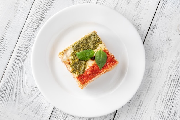 Porción de lasaña de ricotta cubierta con salsa de tomate y pesto