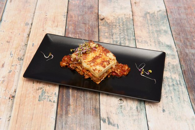 Foto porción de lasaña de ternera con hojas de pasta de carne estofada y bechamel con brotes de soja en un plato negro