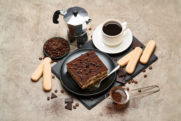 Porción de postre tiramisú italiano tradicional y cafetera moka en mesa de hormigón gris