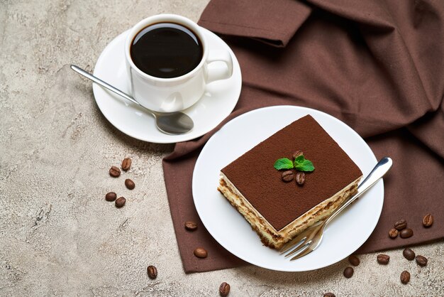 Porción de postre tiramisú italiano tradicional y galletas savoiardi en mesa de hormigón gris