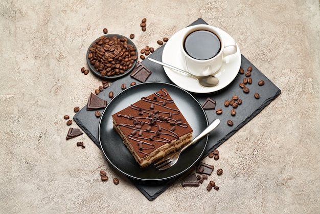 Porción de postre tiramisú italiano tradicional y una taza de café en la mesa de hormigón gris