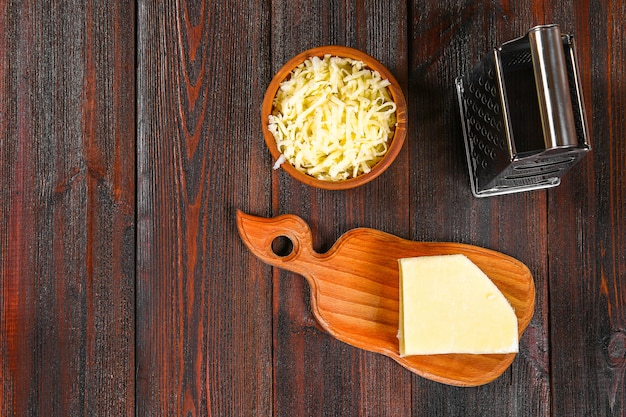 Porción de queso cheddar rallado en la tabla de madera rústica.