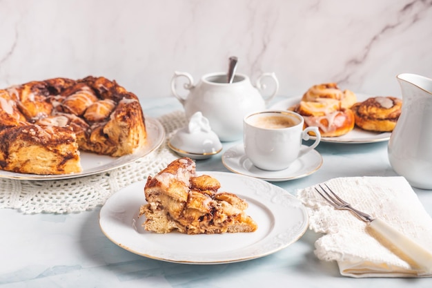 Porción de rollos de canela caseros en un plato blanco sobre una mesa blanca con café y bollos de pastelería