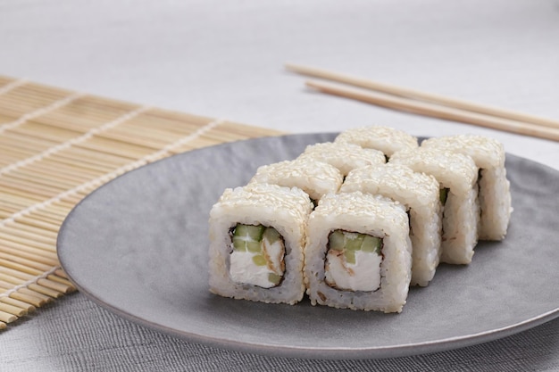 Una porción de rollos en un soporte, comida japonesa, sushi en la mesa, palillos chinos, fondo claro