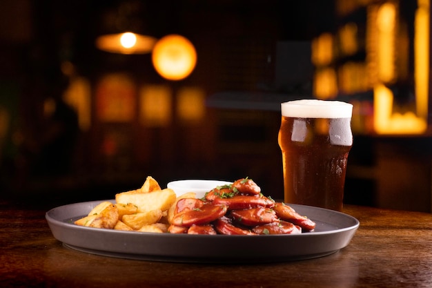 Porción de salchichas bock con papas fritas rústicas y salsa barbacoa y una pinta de curry de pale ale en un pub de fondo borroso