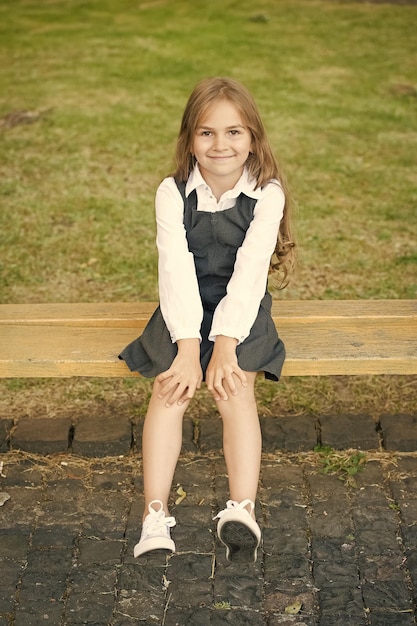 Foto porque su pequeño lo merece. niño feliz sentado en un banco al aire libre. mirada escolar de niña. moda formal. vestido uniforme. educación primaria. cuidado infantil y infancia. día internacional de la infancia.