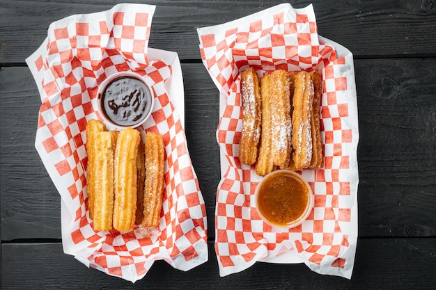 Porras españolas. Comida española como churros españoles con chocolate y caramelo en bandeja de papel, sobre fondo de mesa de madera negra, vista superior plana