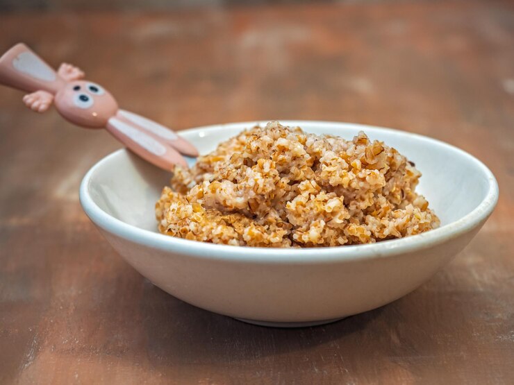Foto porridge de trigo para uma criança em um prato branco profundo e com uma colher de bebê com um punho em forma de lebre
