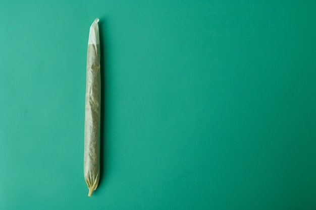 Un porro enrollado de cannabis en un fondo verde en un estudio plano.