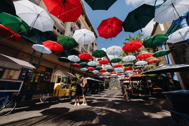 Port Louis, Mauricio, una pareja vestida de negro se encuentra en un callejón de la ciudad cubierta de paraguas que conduce a la capital