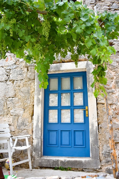 Porta de madeira azul da casa de pedra, cadeira velha. Cacho de uvas verdes dependentes acima