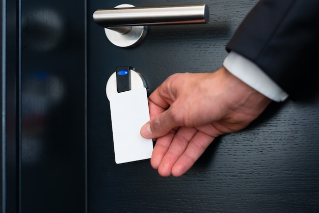 Porta do hotel - Jovem segurando um cartão eletrônico em frente ao sensor eletrônico da porta de um quarto