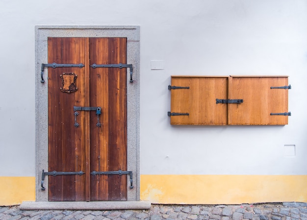 Porta dupla de madeira velha na parede branca concreta com pequena janela de madeira ao lado