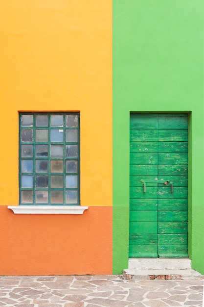 Porta e janela verdes na fachada pintada de verde-amarelo da casa. Arquitetura colorida na ilha de Burano, Veneza, Itália.