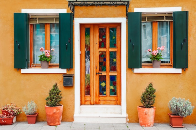 Porta e janelas com flores na fachada amarela da casa. Arquitetura colorida na ilha de Burano, Veneza, Itália.