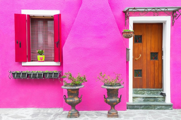 Porta e janelas com flores na fachada rosa da casa. Arquitetura colorida na ilha de Burano, Veneza, Itália.