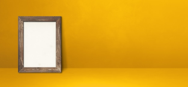 Porta-retrato de madeira encostado em uma parede amarela. Modelo de maquete em branco. Banner horizontal