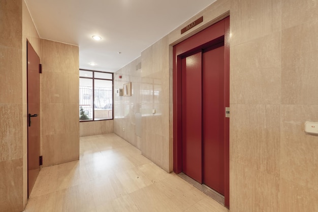 Portal de una casa con baldosas y suelos de mármol y un ascensor con puertas de metal rojo