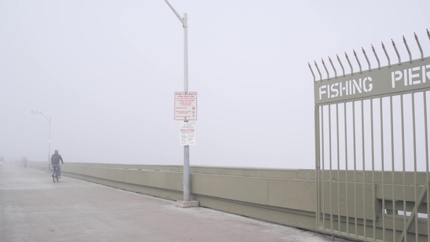 Portão de metal do cais da praia oceânica na entrada do calçadão enevoado da neblina, costa da califórnia