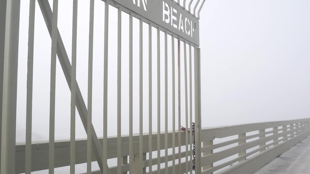 Portão de metal do cais da praia oceânica na entrada do calçadão enevoado da neblina, costa da califórnia