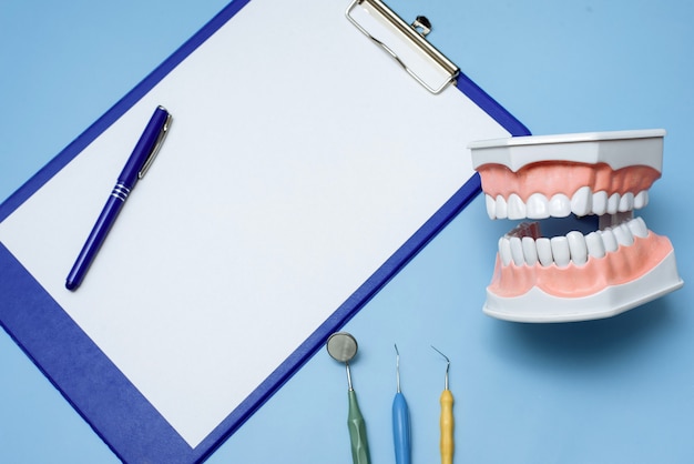 Foto portapapeles azul, modelo dental e instrumentos de dentista sobre fondo azul.