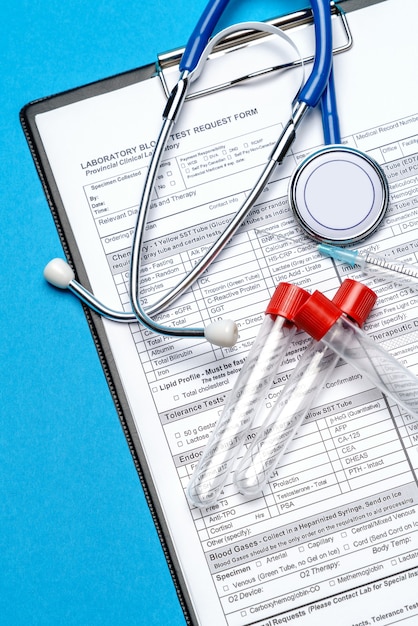 Portapapeles con formulario de papel en blanco con herramientas médicas sobre fondo azul con espacio para hacer frente.