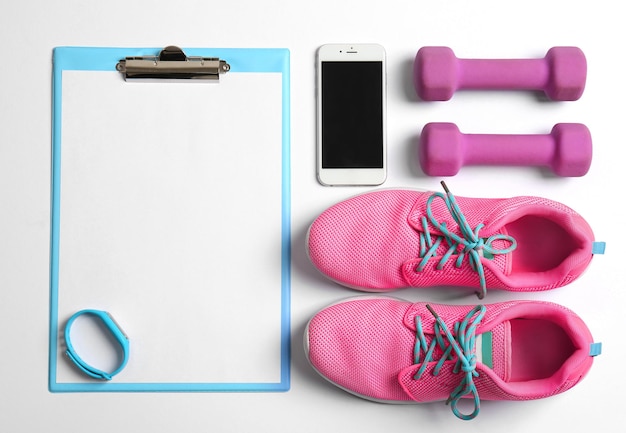 Foto portapapeles con papel en blanco para el plan de ejercicios cosas de gimnasio y teléfono móvil sobre fondo blanco composición plana