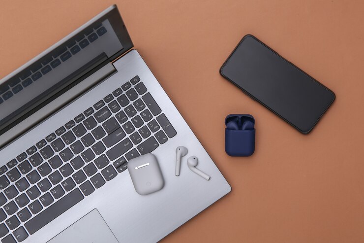 Foto portátil y auriculares inalámbricos con estuche cargador y smartphone sobre fondo marrón. vista superior